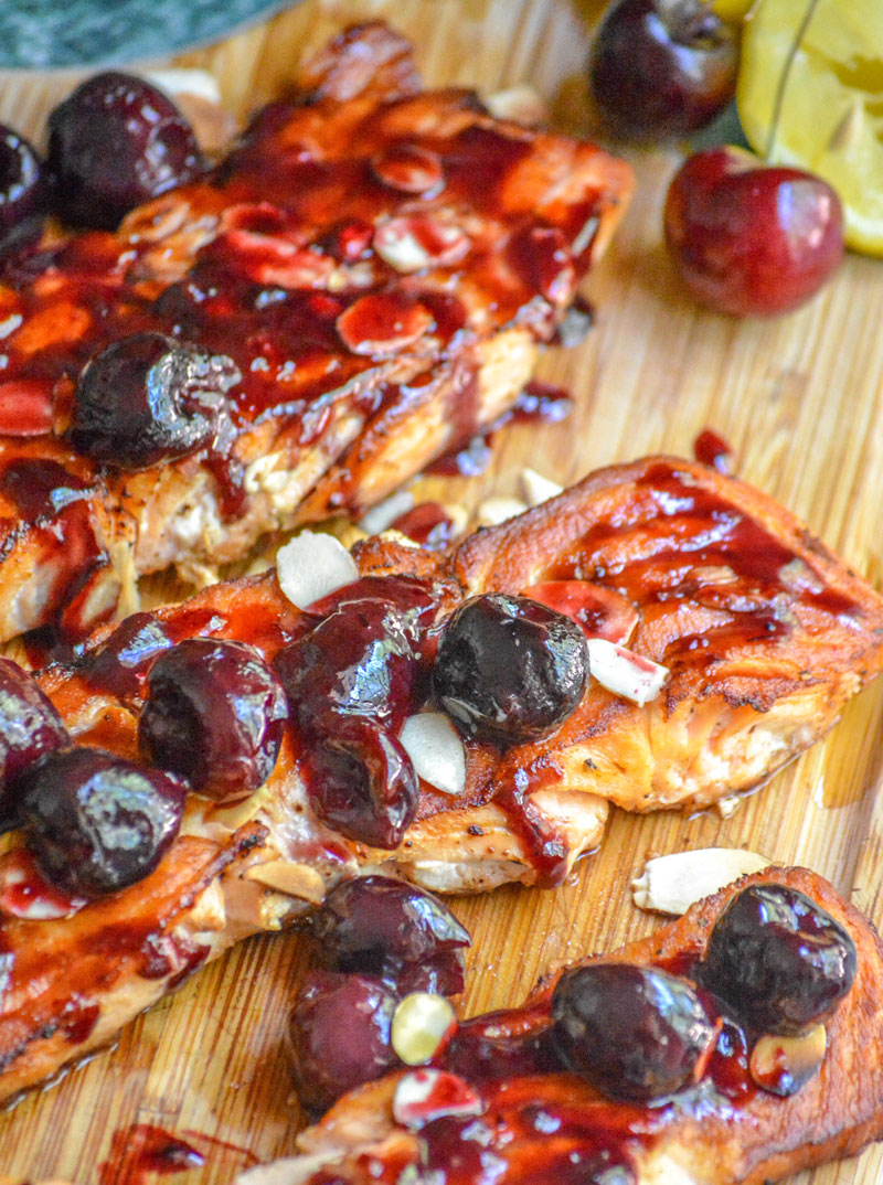 PIECES OF PAN SEARED SALMON TOPPED WITH FRESH CHERRY ALMOND SAUCE ON A WOODEN CUTTING BOARD