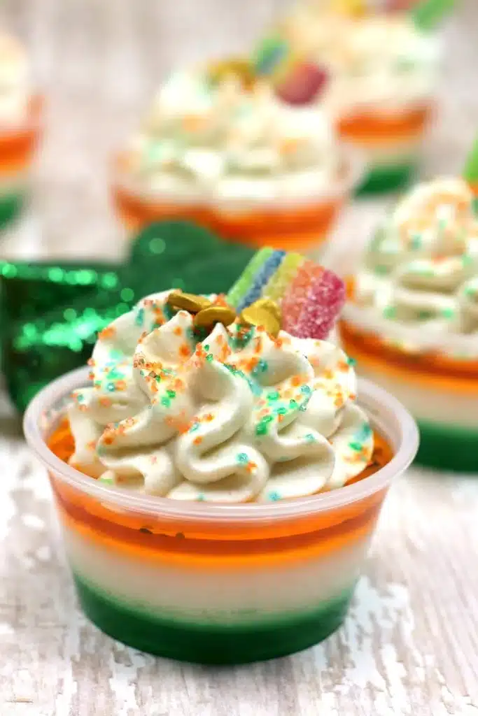 LUCK OF THE IRISH JELLO SHOTS TOPPED WITH WHIPPED CREAM AND SPRINKLES ON A WOODEN TABLE