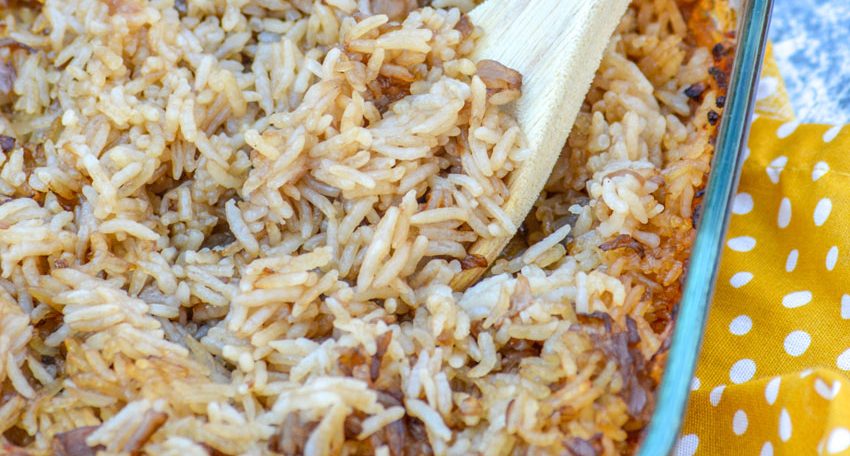 A WOODEN SPOON SCOOPING STICK OF BUTTER RICE OUT OF A GLASS BAKING DISH