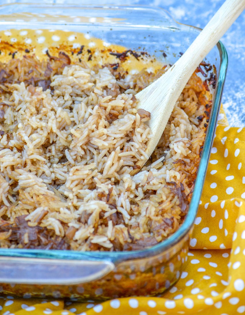 A WOODEN SPOON SCOOPING STICK OF BUTTER RICE OUT OF A GLASS BAKING DISH