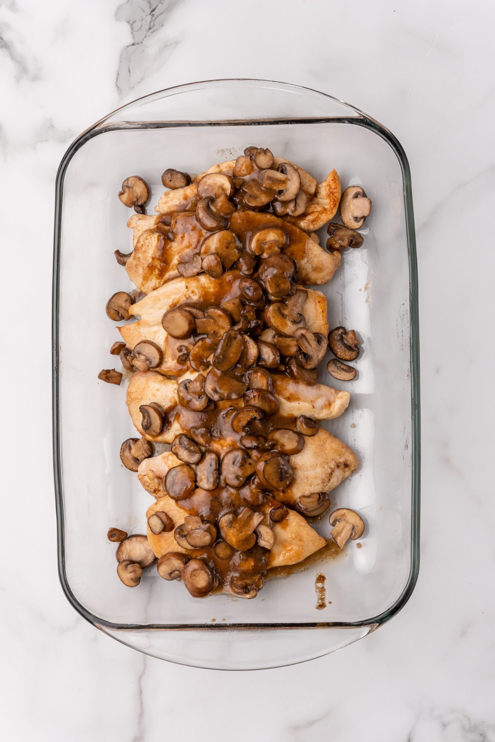 chicken cutlets covered with sauteed mushrooms in a glass baking dish