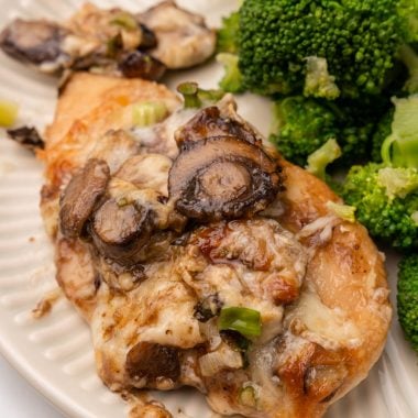 a piece of chicken lombardy next to steamed broccoli on a white plate