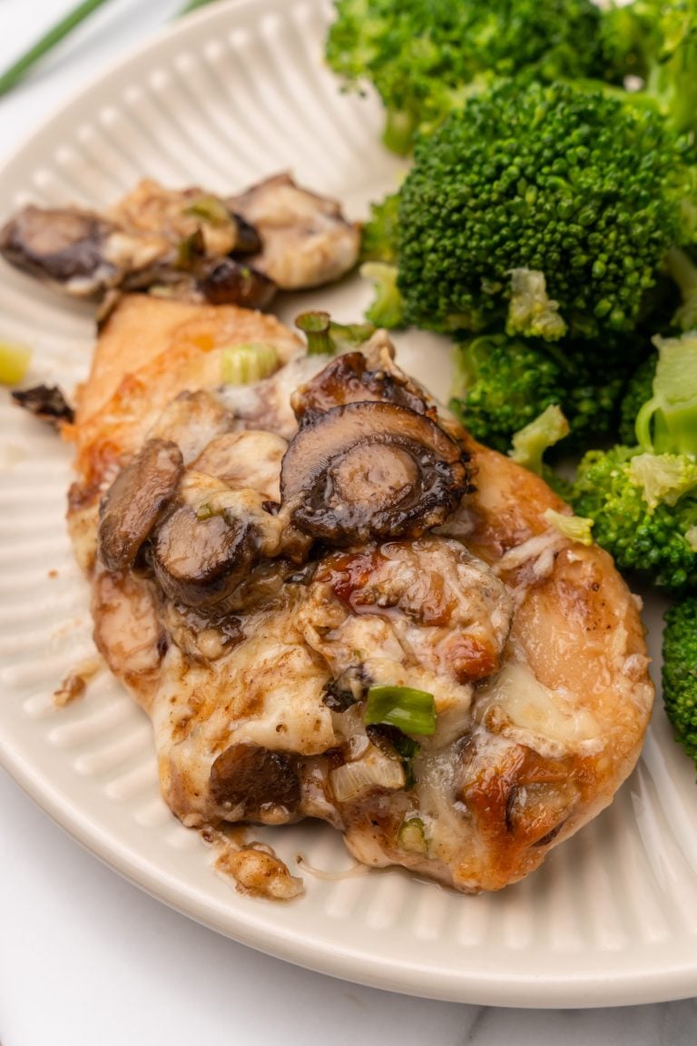 a piece of chicken lombardy next to steamed broccoli on a white plate