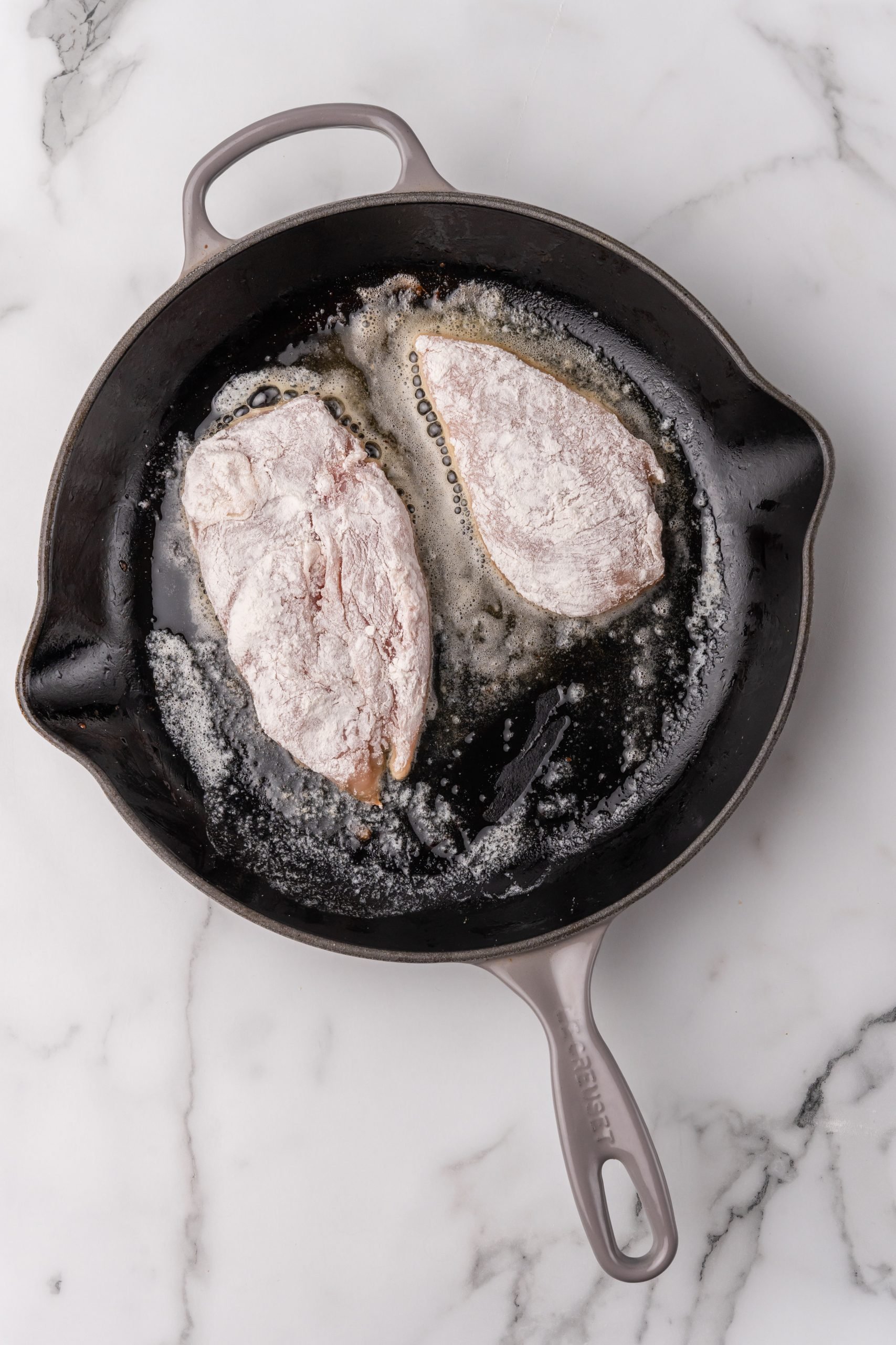 floured chicken cutlets in a black skillet with oil
