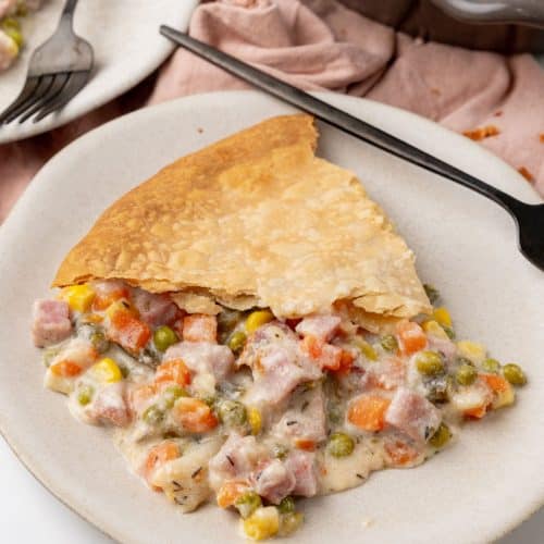 a slice of vegetable cobbler with ham on a white plate with a black fork resting on the side