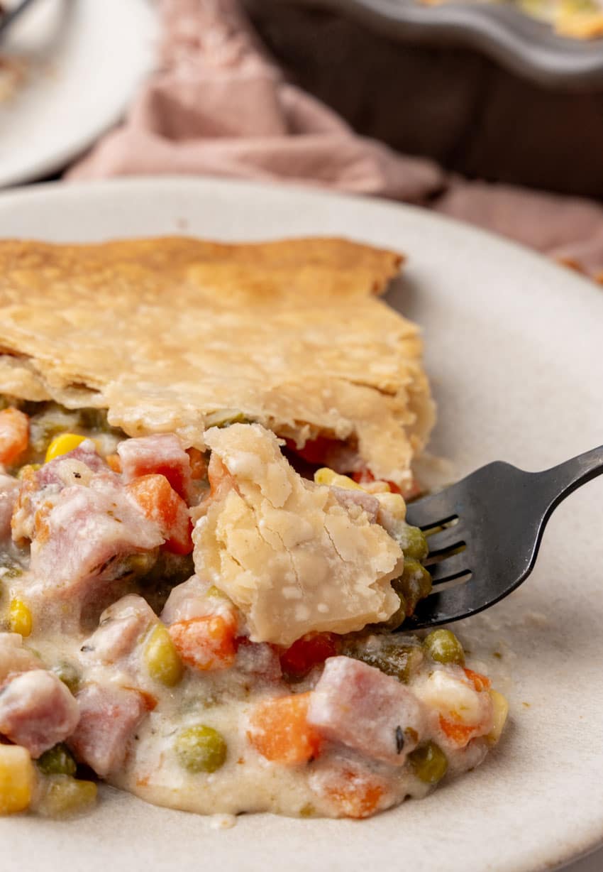 a black fork lifting a scoop of ham cobbler off a white plate