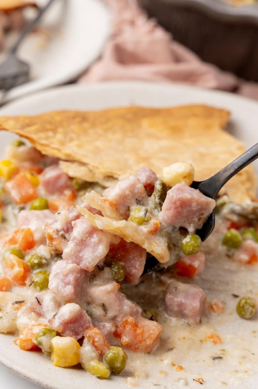 a black fork lifting a scoop of ham cobbler off a white plate