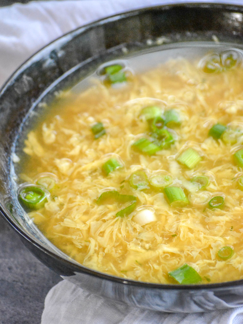 A BOWL OF EGG DROP SOUP ON A WOODEN TABLE