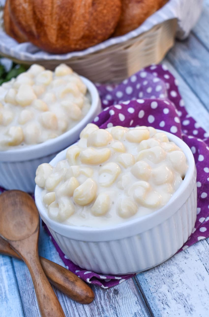 white cheddar mac and cheese in two white ramekins with a basket of crusty rolls in the background