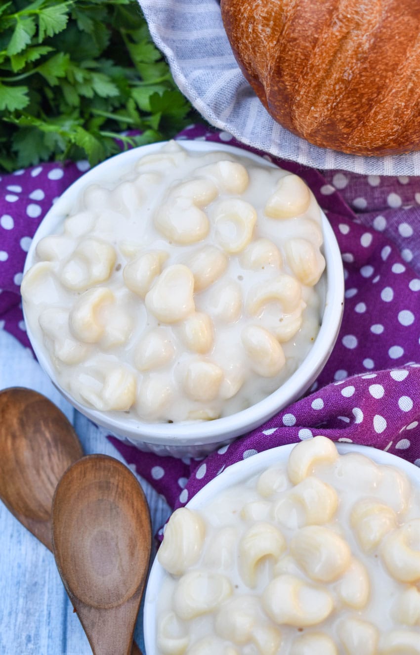 white cheddar mac and cheese in two white ramekins with a basket of crusty rolls in the background