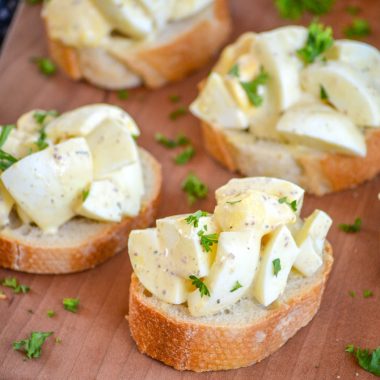 DEVILED EGG BRUSCHETTA ON THICK SLICES OF BAGUETTE BREAD ON A WOODEN CUTTING BOARD