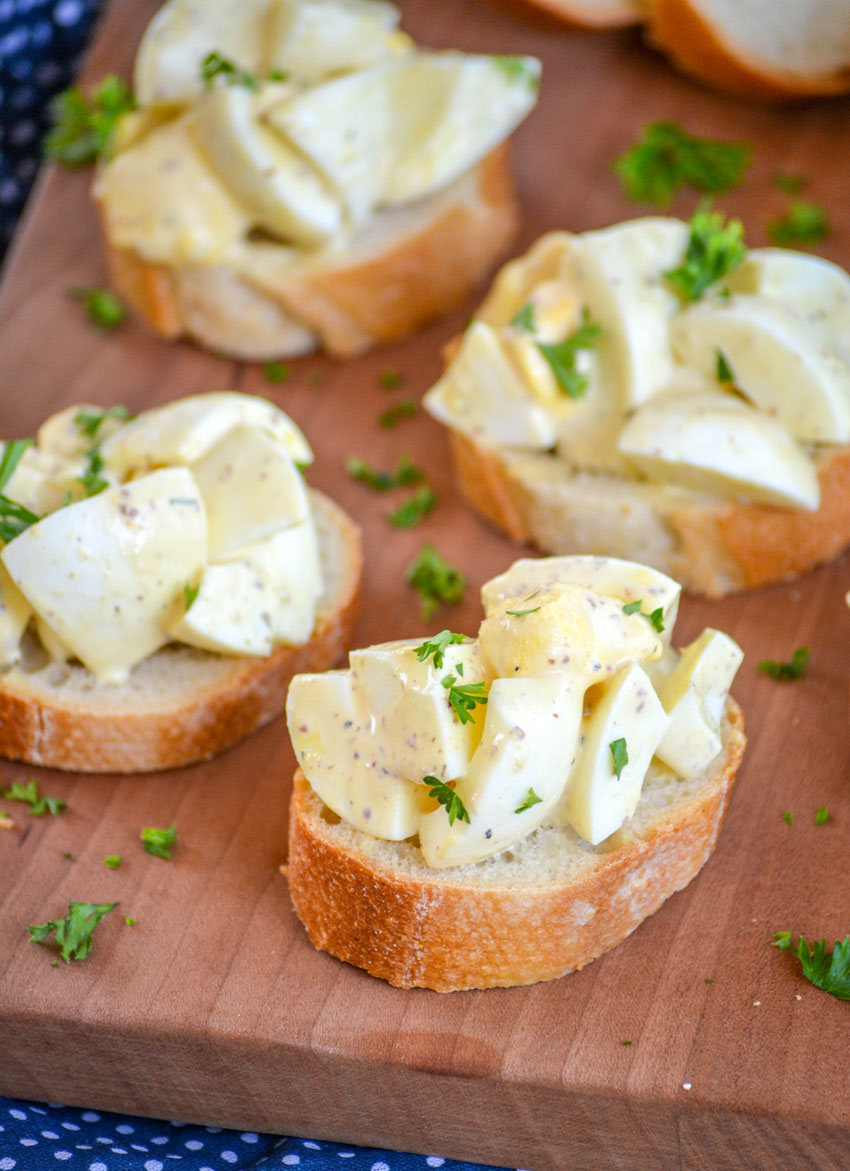 DEVILED EGG BRUSCHETTA ON THICK SLICES OF BAGUETTE BREAD ON A WOODEN CUTTING BOARD