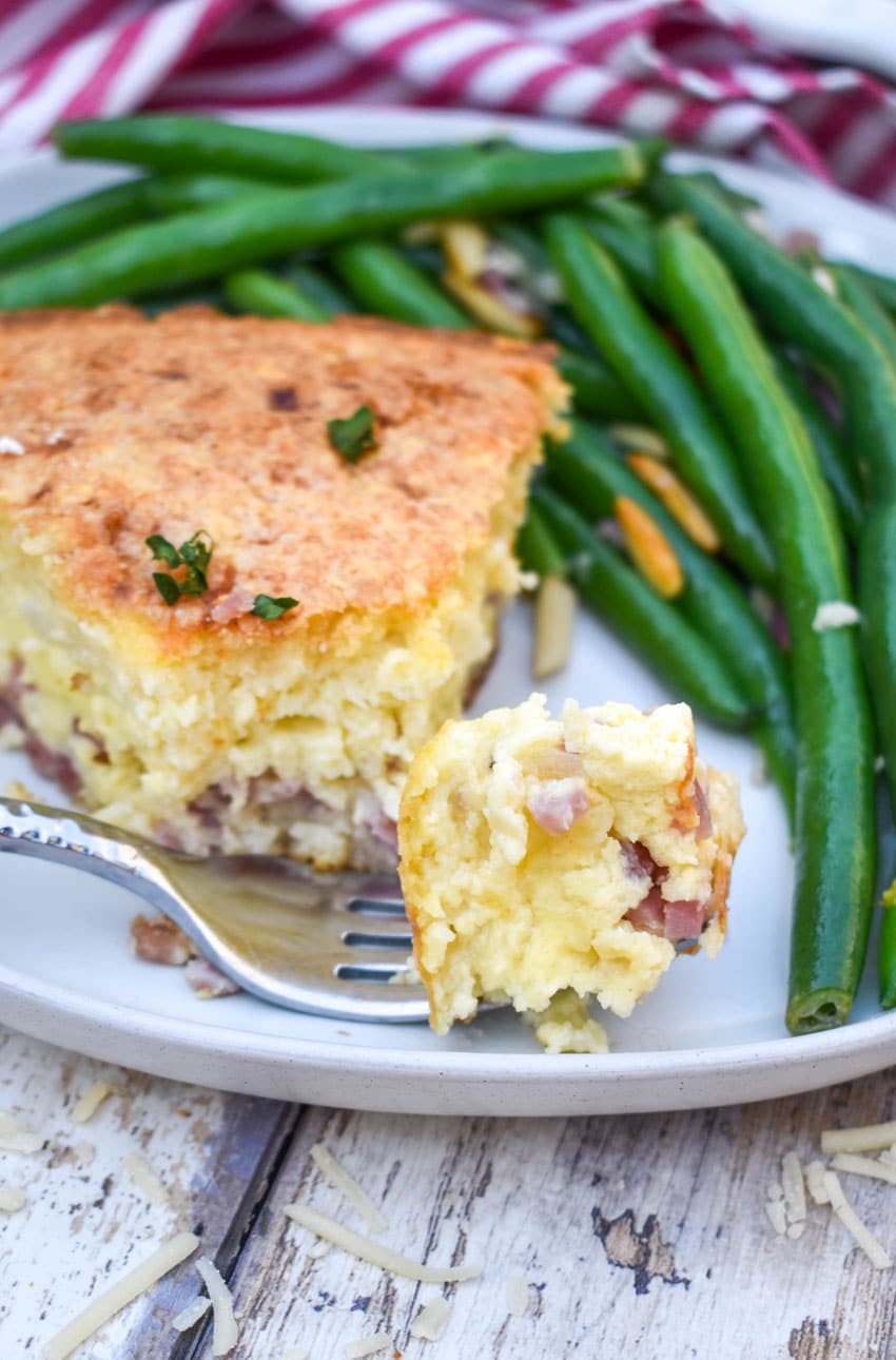 a silver fork resting on a white plate holding a piece of ham and swiss pie