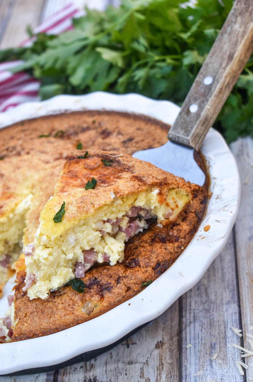 a wooden spatula holding up a slice of ham and swiss pie