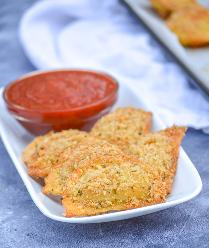 Oven Baked Toasted Ravioli on a white platter with an appetizer bowl of marinara sauce for dipping