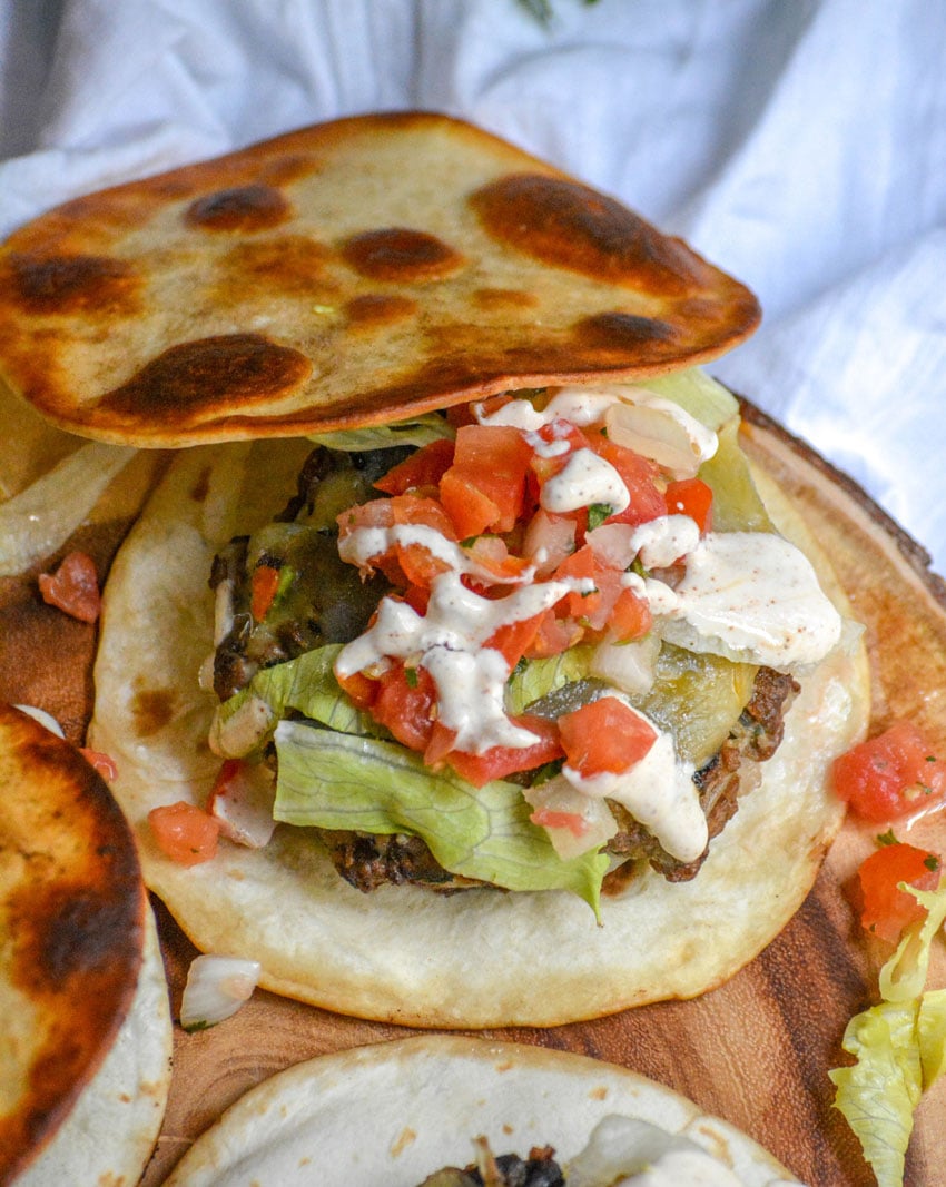 A QUESADILLA BUBRGER RESTING ON A WOODEN CUTTING BOARD