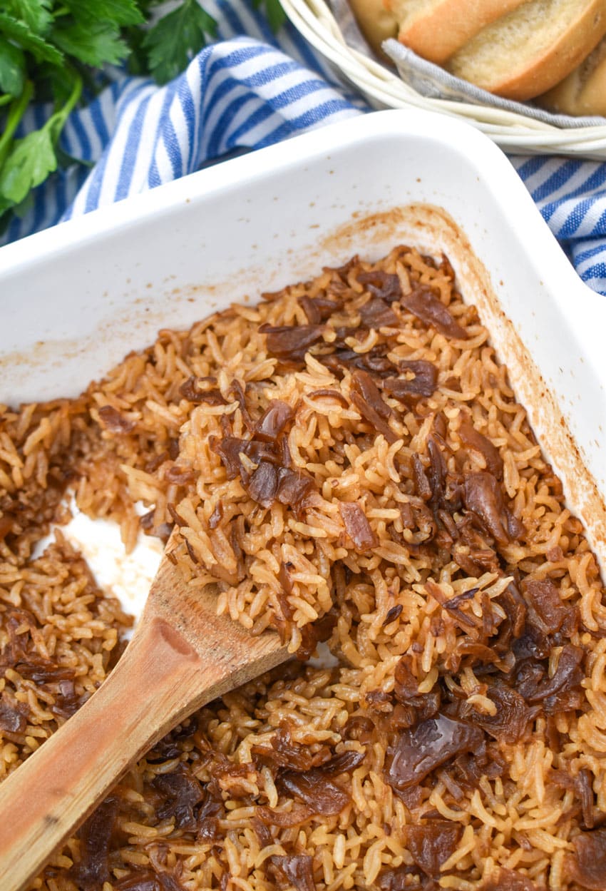 a wooden spoon scooping no peek rice out of a white baking dish