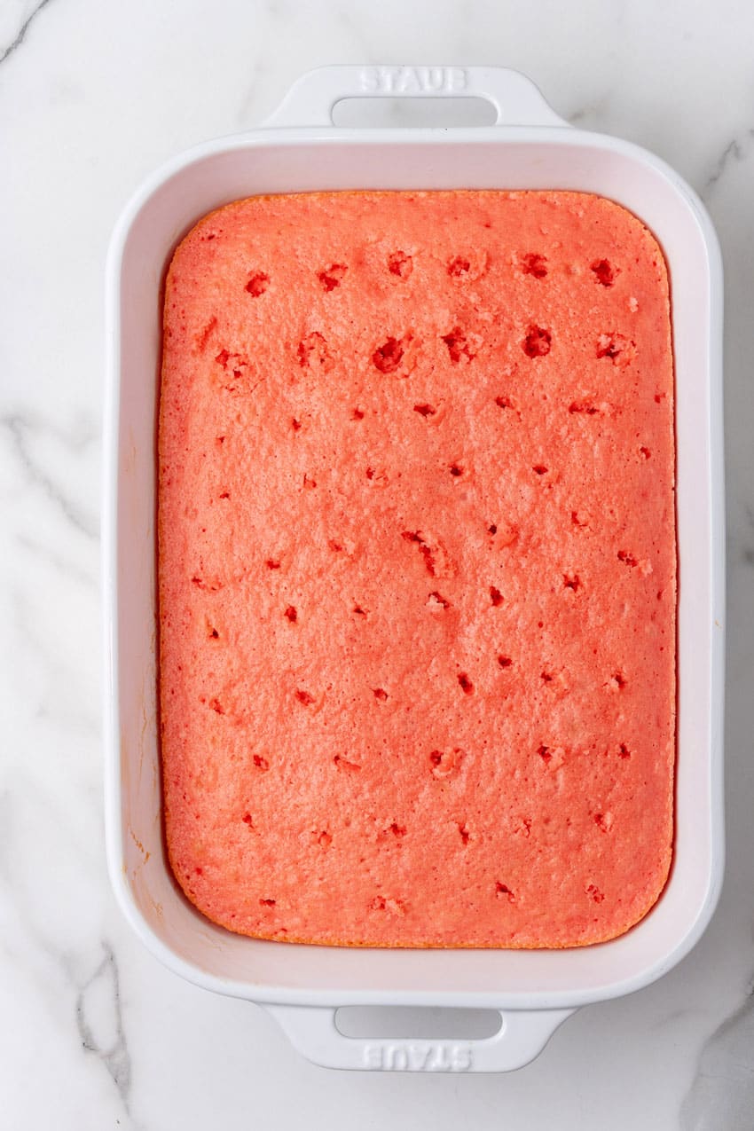 a baked strawberry cake with holes poked all over the surface