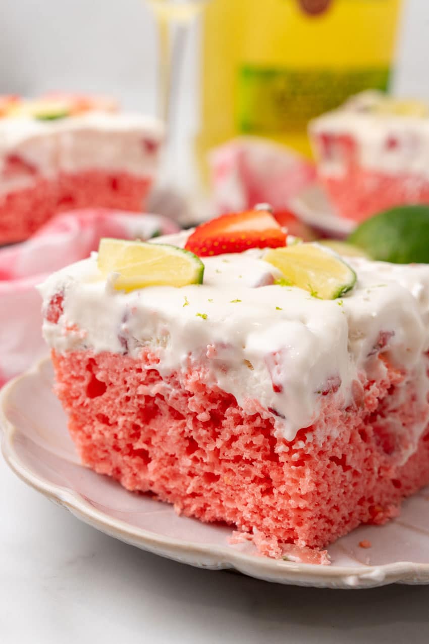 slices of strawberry margarita poke cake on small white dessert plates