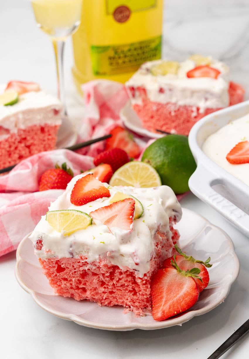 slices of strawberry margarita poke cake on small white dessert plates