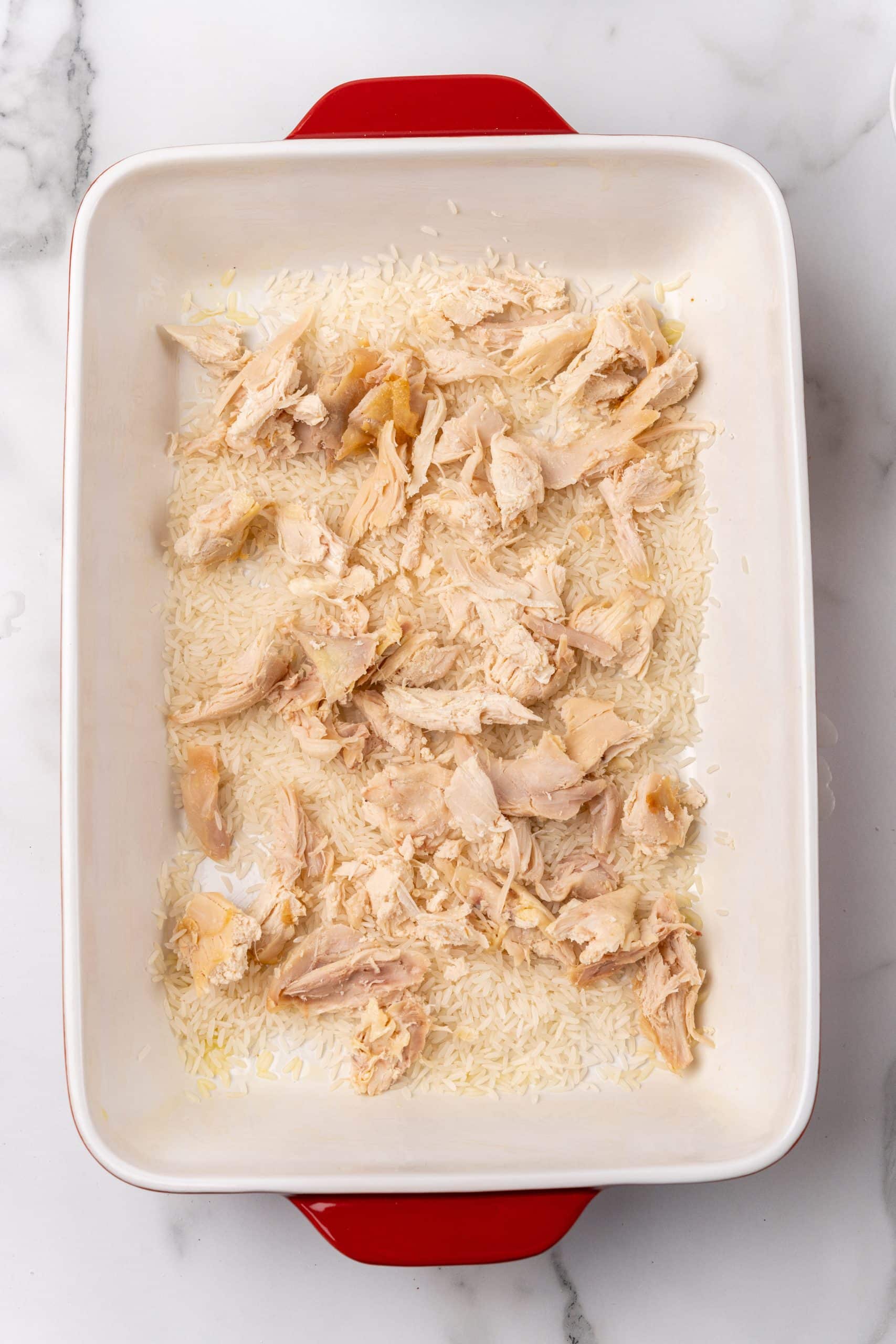 pieces of rotisserie chicken spread over uncooked rice in a large casserole dish