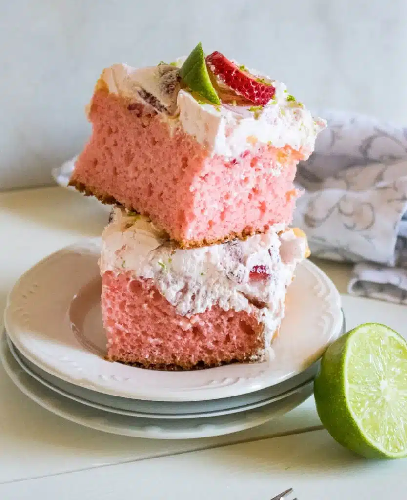 TWO SLICES OF STRAWBERRY LIME TEQUILA POKE CAKE STACKED TOGETHER ON A WHITE DESSER PLATE