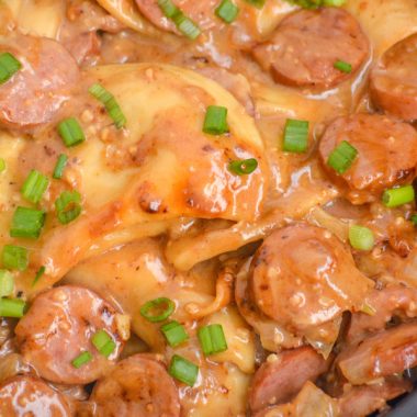 CREAMY SMOKED SAUSAGE AND PIEROGI TOPPED WITH SLICED GREEN ONIONS IN A BLACK SKILLET