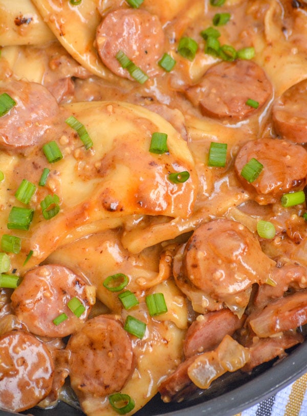 CREAMY SMOKED SAUSAGE AND PIEROGI TOPPED WITH SLICED GREEN ONIONS IN A BLACK SKILLET