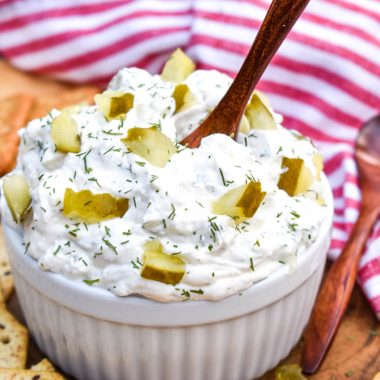 a wooden spoon stuck in creamy dill pickle dip in a small white bowl