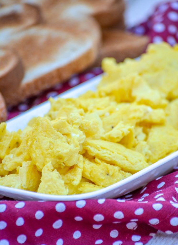 the perfect scrambled eggs every time these are piled high on a white platter with crispy browned slices of toast in the background