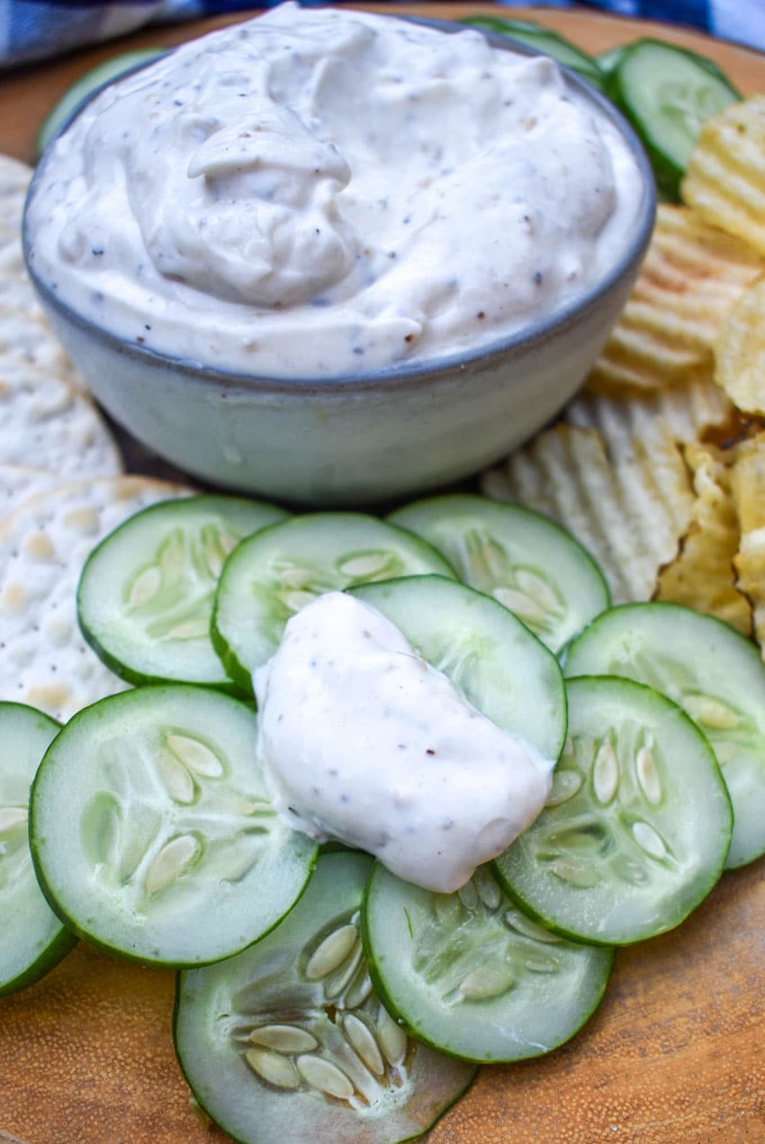 a cucumber sliced topped with montreal steak seasoning dip on a pile of sliced cucumbers