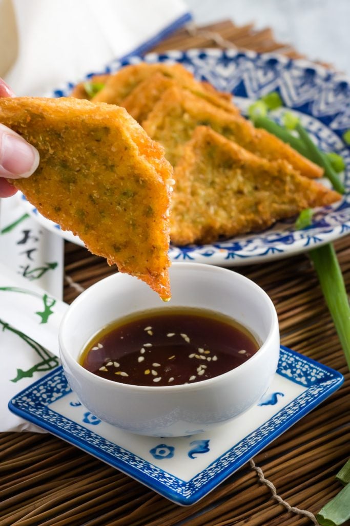Shrimp Toast Recipe layered on a blue and white oriental style plate on a bamboo cutting board with one piece shown above a dipping bowl of soy sauce
