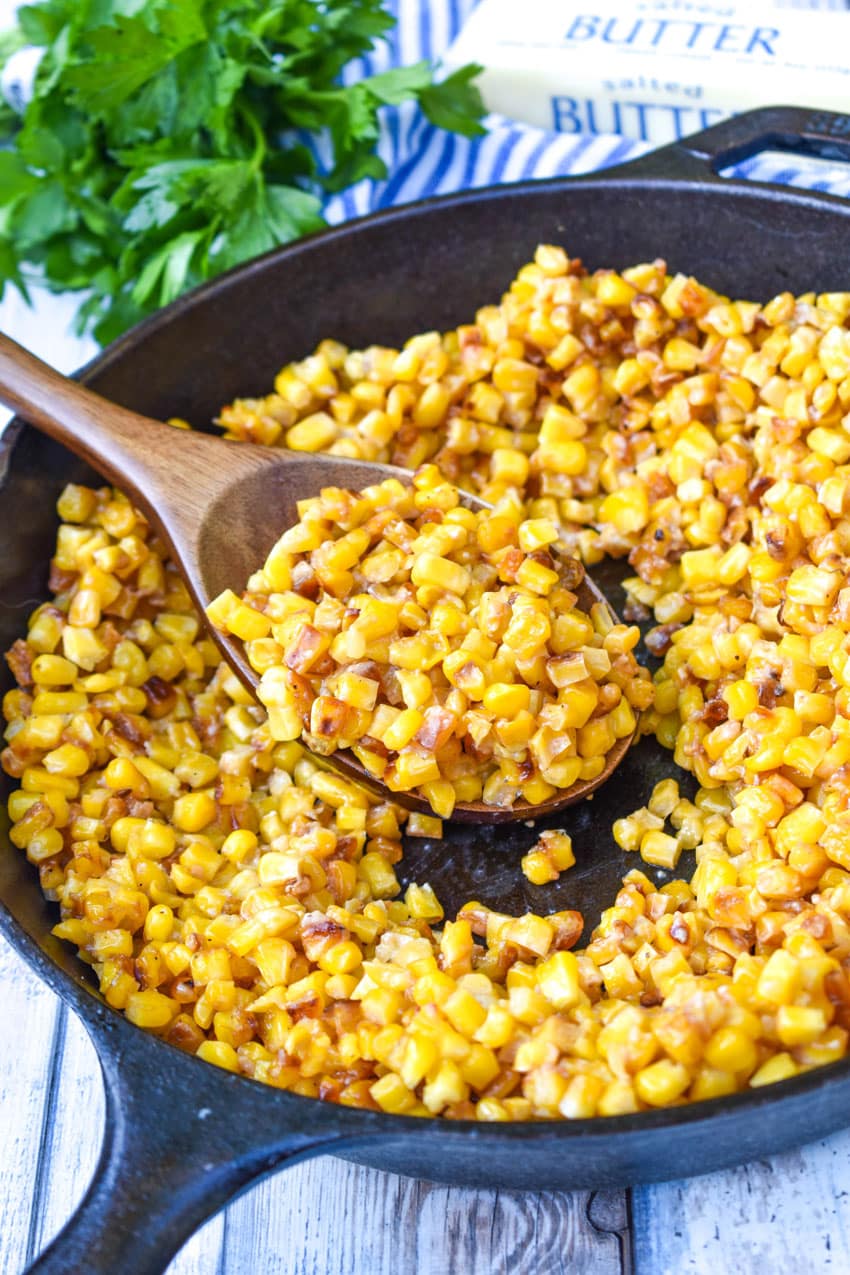 a wooden spoon in a black skillet filled with a southern fried corn recipe