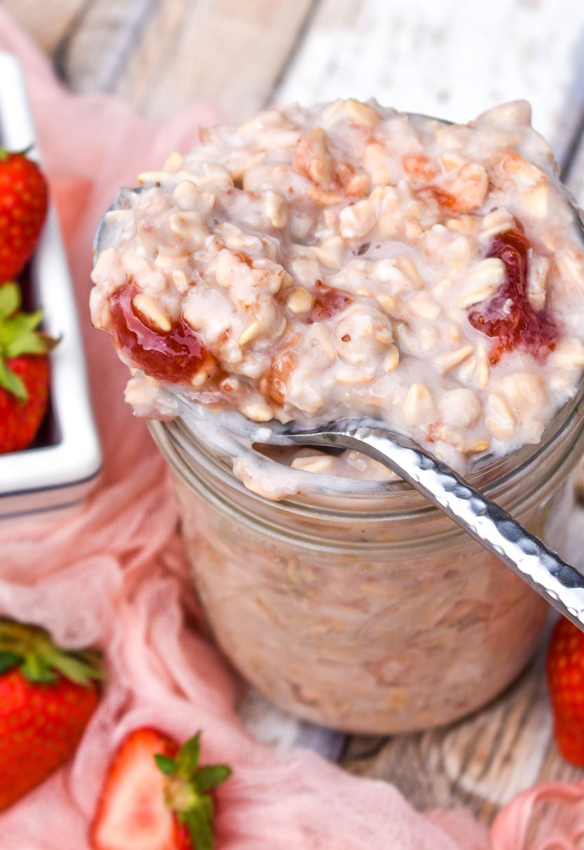 a silver spoon digging into a jar of strawberries and cream overnight oats