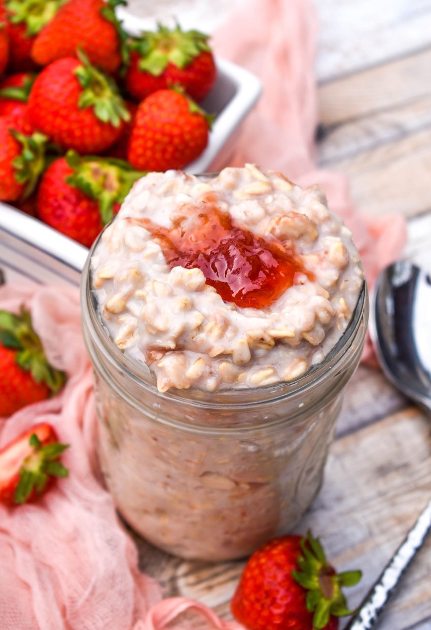 strawberries and cream overnight oatmeal in a glass mason jar topped with a dollop of strawberry jam