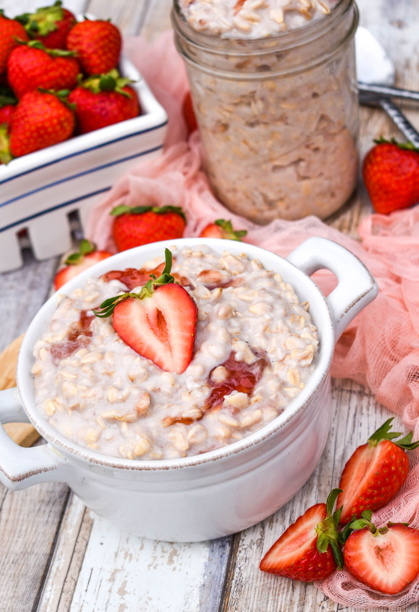strawberries and cream overnight oats on a white bowl surrounded by fresh berries