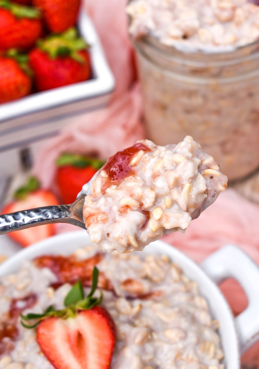 a silver spoon holding up a spoonful of strawberry cream overnight oats