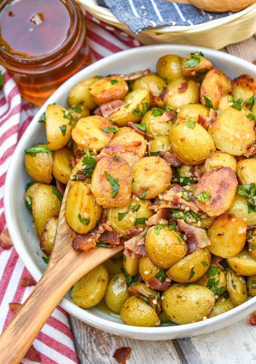 a wooden spoon scooping warm honey mustard potato salad out of a white serving bowl