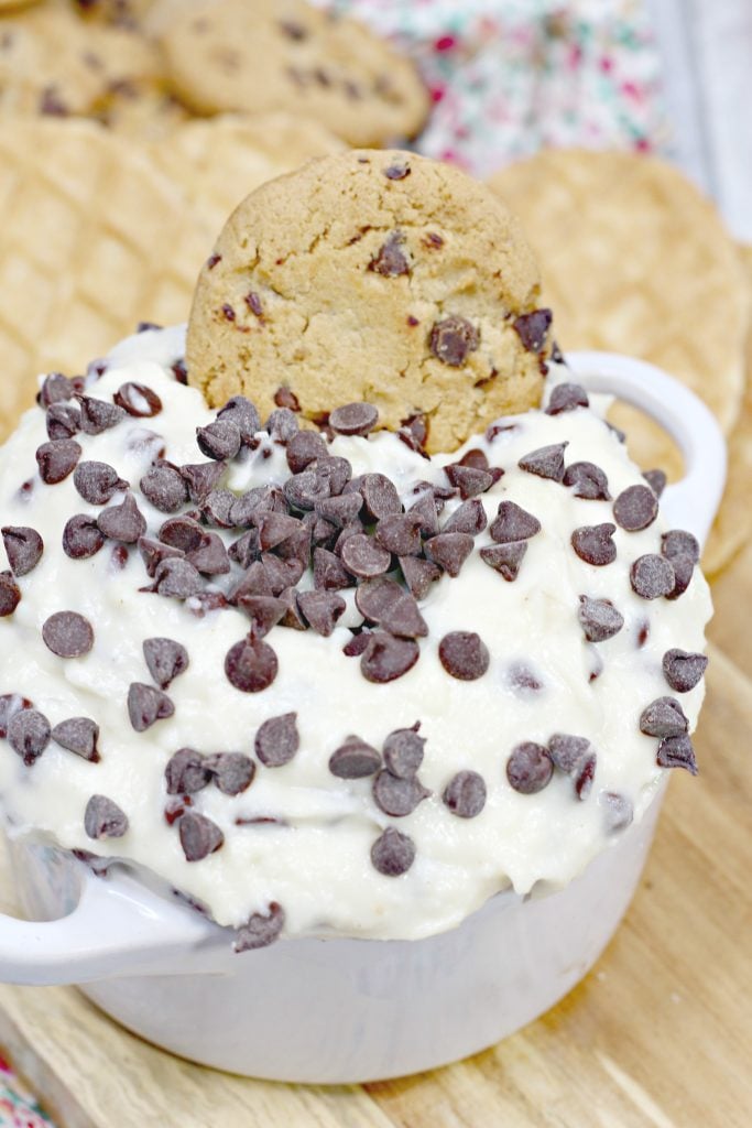 cannoli dip in a bowl is studded with chocolate chips with a cookie stuck in the center for garnish