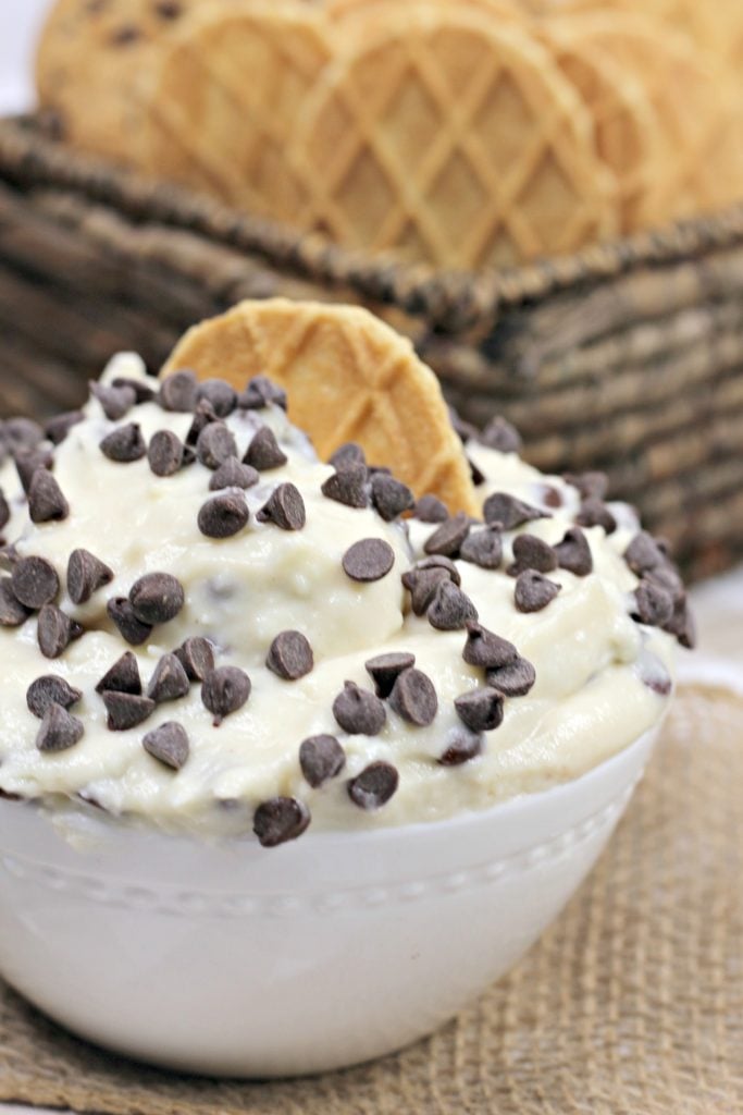 a sweet Italian style cannoli cream dip in a bowl, studded with mini chocolate chips with Belgian waffle cookies in the back ground