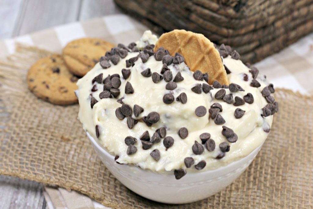 Nonna's Italian cannoli dip piled high in a white bowl, sprinkled with miniature chocolate chips, and garnished with a Belgian waffle cookie