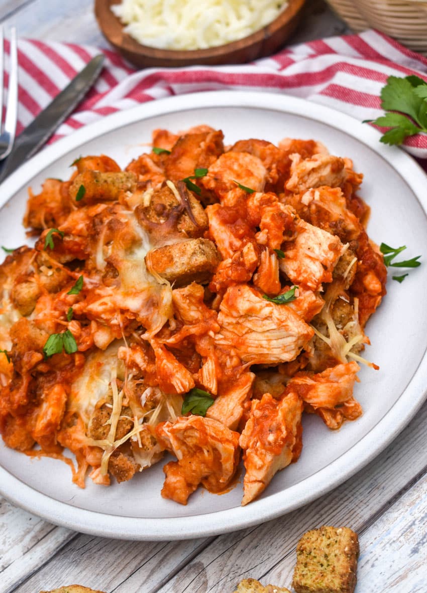 chicken parmesan casserole on a white plate next to fresh green leafy herbs
