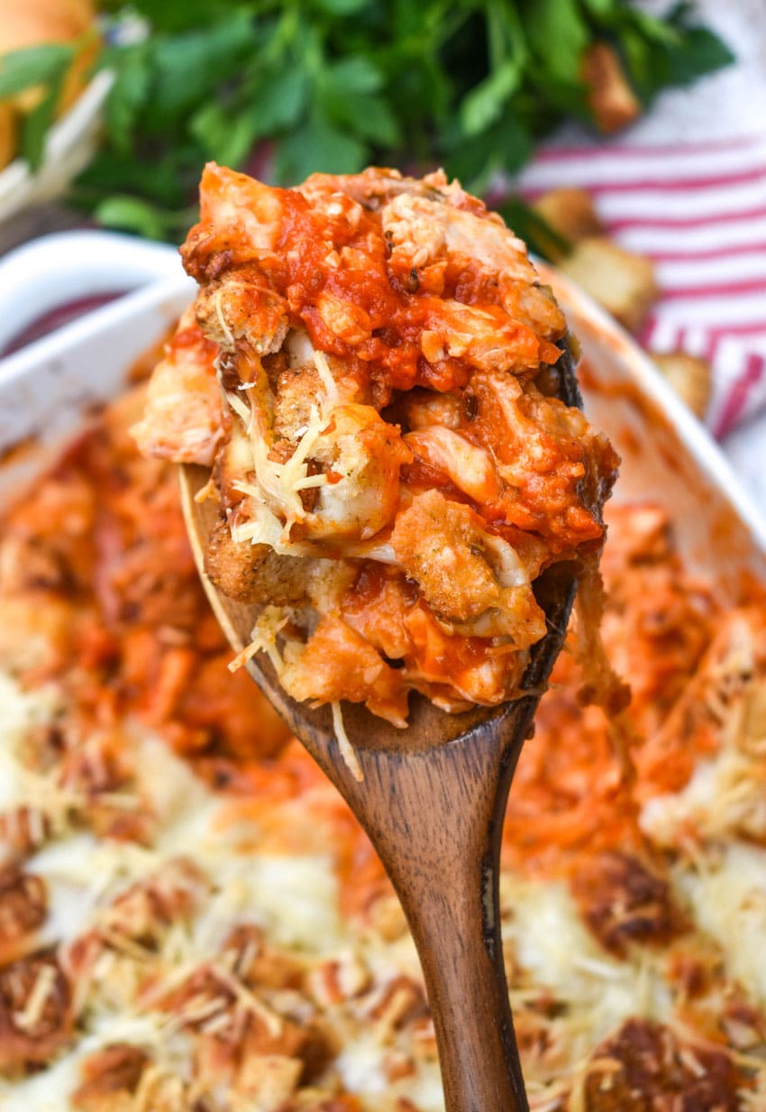 a wooden spoon holding up a scoop of baked chicken parmesan casserole