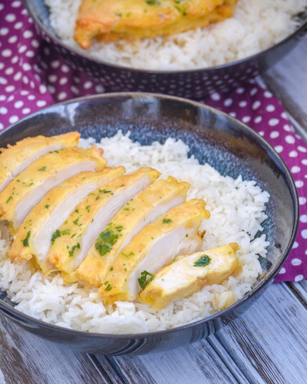 A SLICED PIECE OF COPYCAT CHICKEN FRENCH FROM WEGMAN'S OVER A BED OF STEAMED WHITE RICE IN A BLUE BOWL