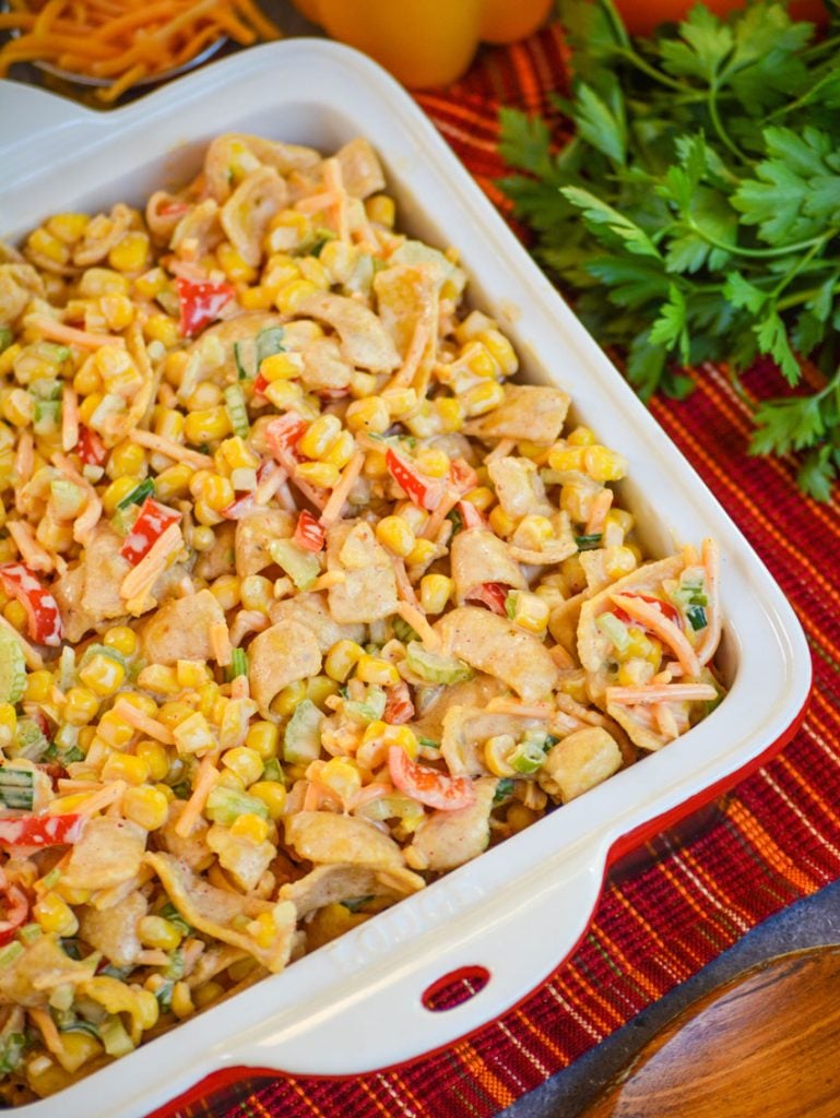 crunchy corn salad in a square ceramic dish with fresh cilantro and shredded cheddar in the background