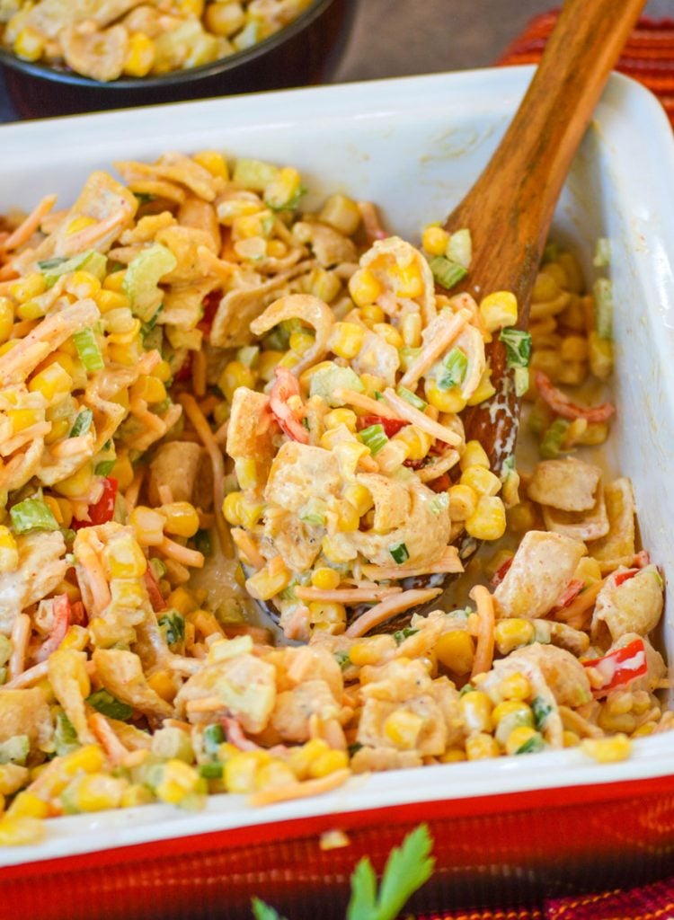 fritos corn salad being scooped out of a dish with a large wooden spoon