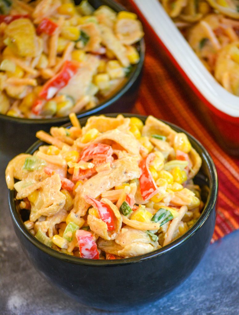 a black bowl of crunchy corn salad studded with brightly colored pieces of sweet pepper, corn kernels, corn chips, shredded cheddar, and sliced green onions