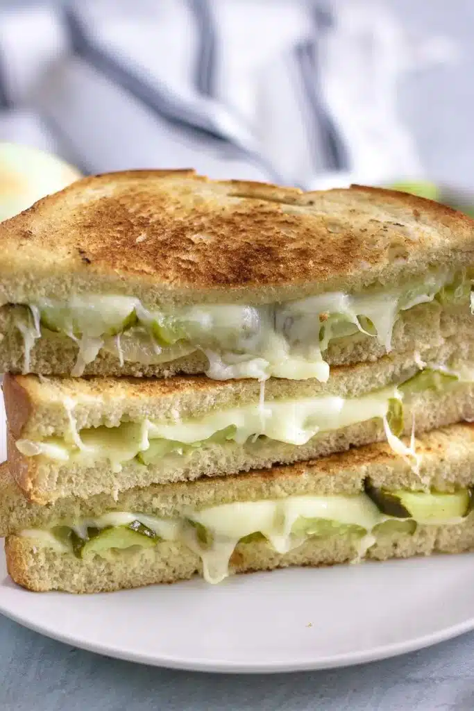 SLICES OF DILL PICKLE GRILLED CHEESE STACKED TOGETHER ON A WHITE PLATE