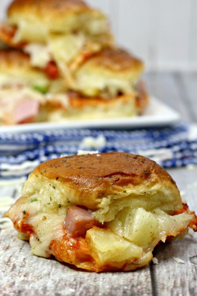 a single Hawaiian slider is shown in the foreground with juicy pineapple and savory ham showing from the sandwich