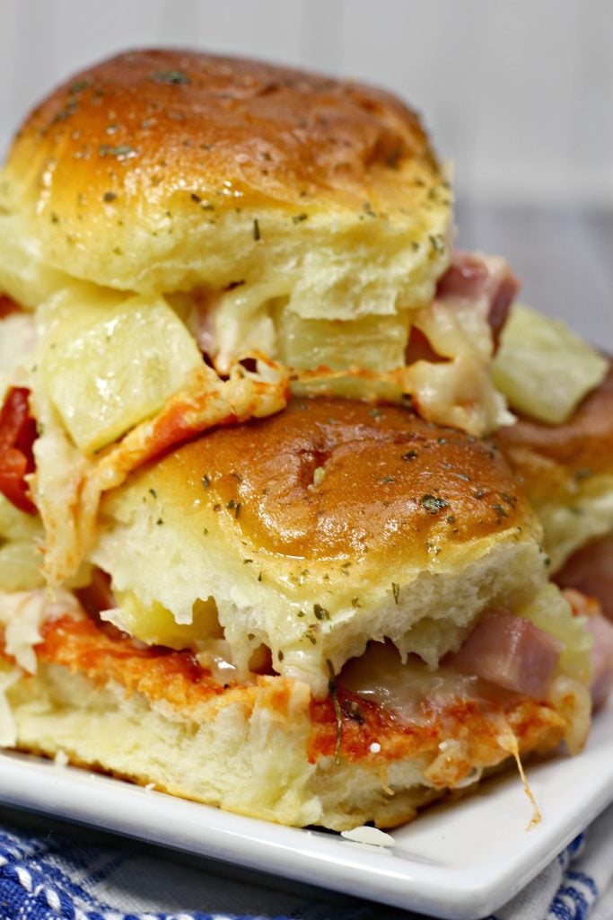 Hawaiian pizza sliders are pictured glistening from the savory butter glaze on top of the buns with a sprinkle of seasonings